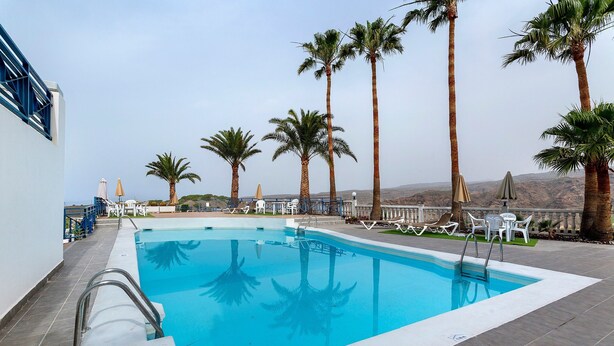 A swimming pool with palm trees, lounge chairs, and a clear sky. - Vacation Apartment 'Vista Golf' with Sea View, Shared Pool and Wi-Fi (Mogán)