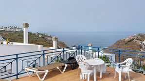A terrace with a table and chairs, a cushioned bench, and a view of the sea. - Vacation Apartment 'Vista Golf' with Sea View, Shared Pool and Wi-Fi (Mogán)
