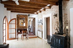 A room with a wooden ceiling, a fireplace, a mirror, and a door leading to another room.
