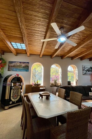 Ein Essbereich mit Tisch und Stühlen, Deckenventilator, Holzbalken und Rundbogenfenstern.