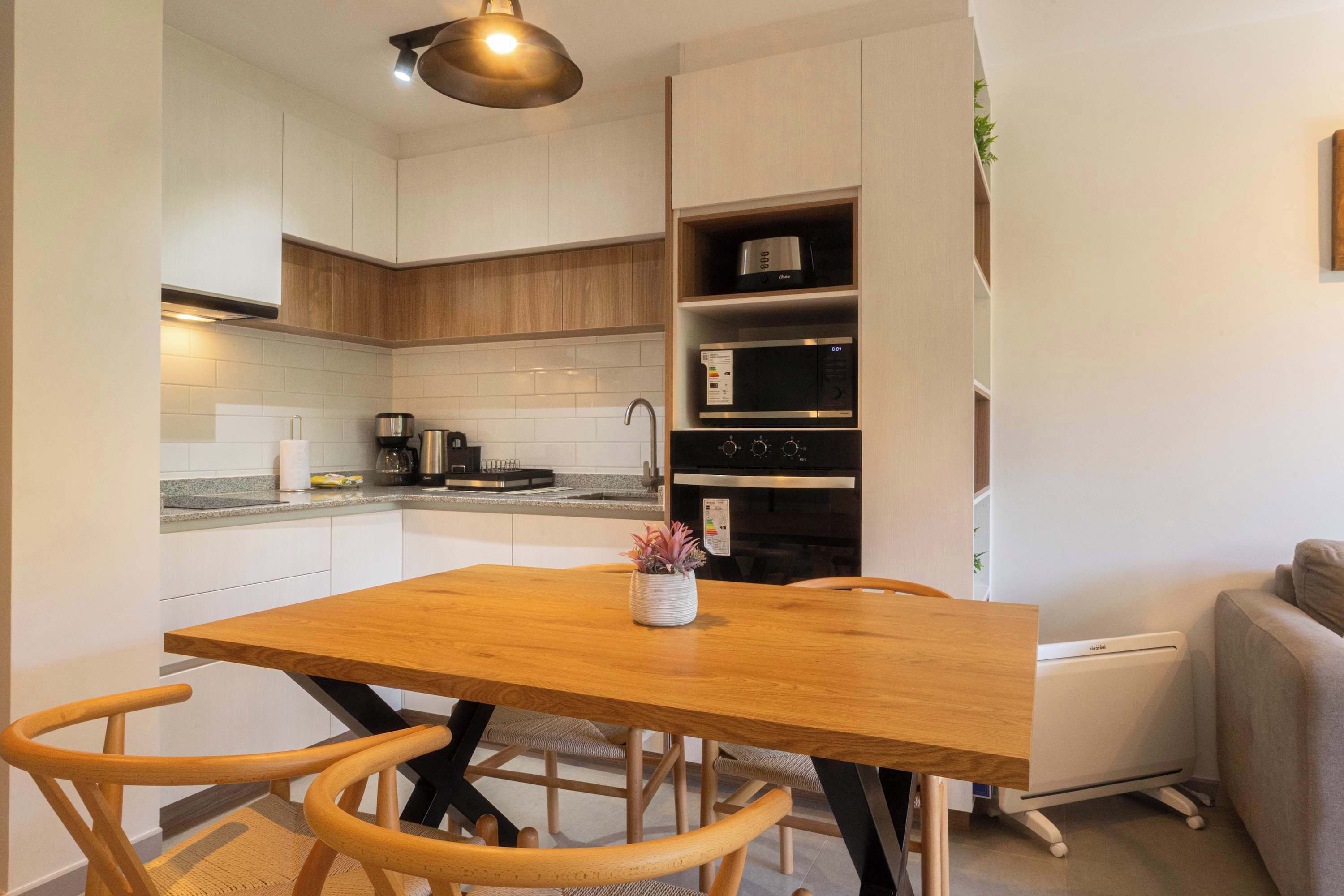 Une cuisine moderne avec des meubles blancs, une table à manger en bois et des appareils électroménagers intégrés.