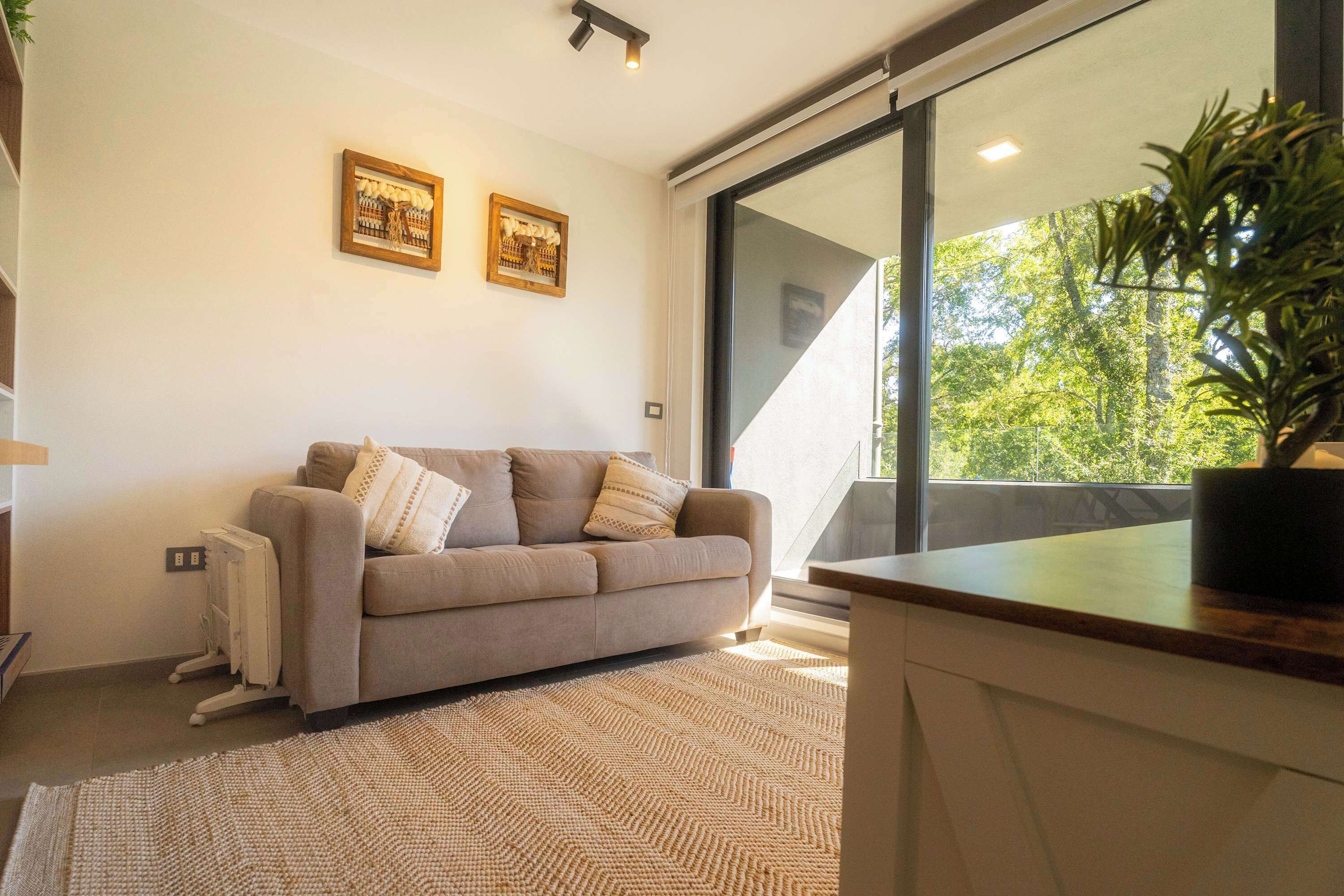 A modern living room with a sofa, a radiator, a large window, and two framed pictures on the wall.