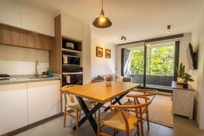 A modern kitchen with a wooden table and chairs, a built-in oven, and a large window offering a view of trees.