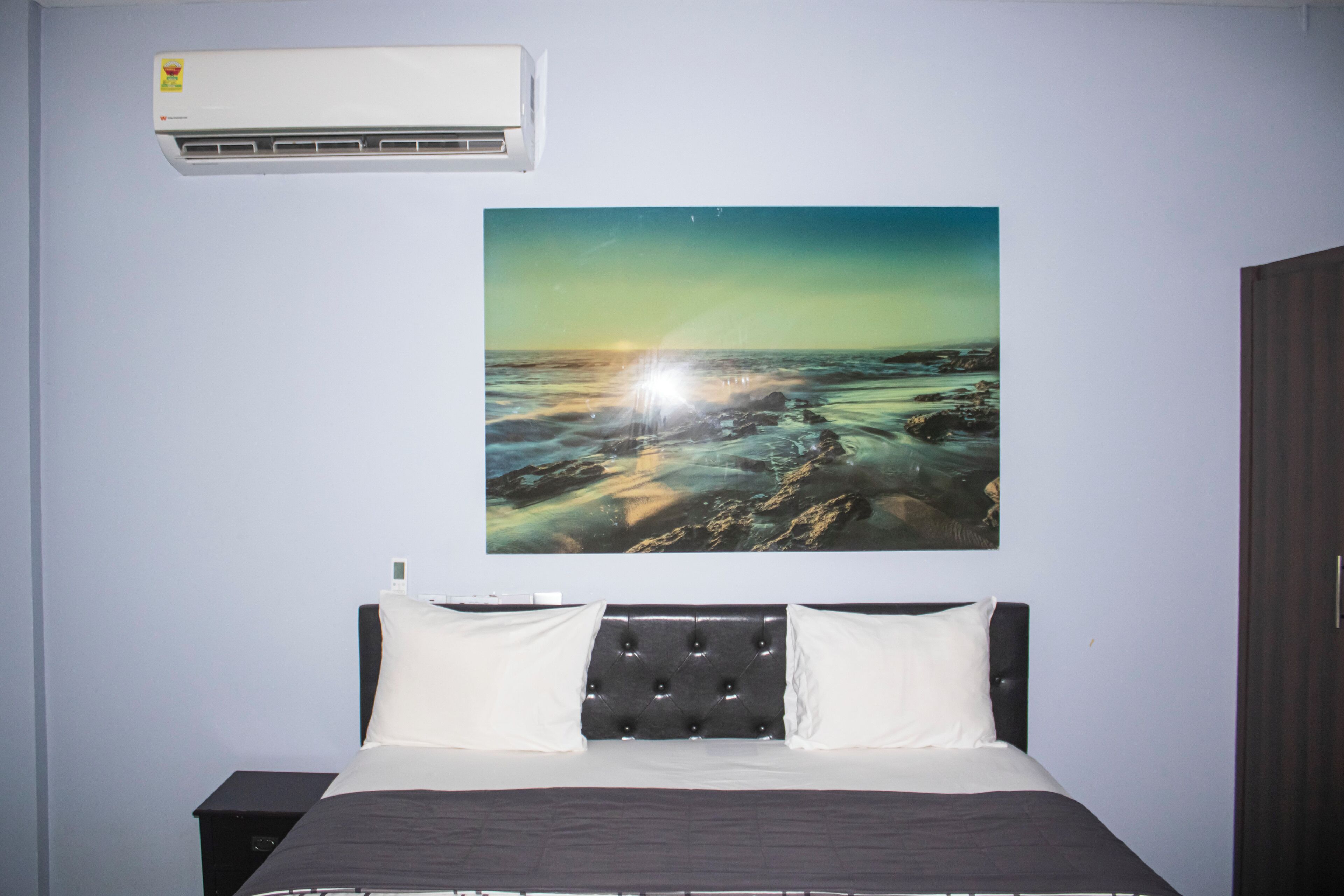 Un dormitorio con una cama, aire acondicionado de pared y un cuadro grande de paisaje.