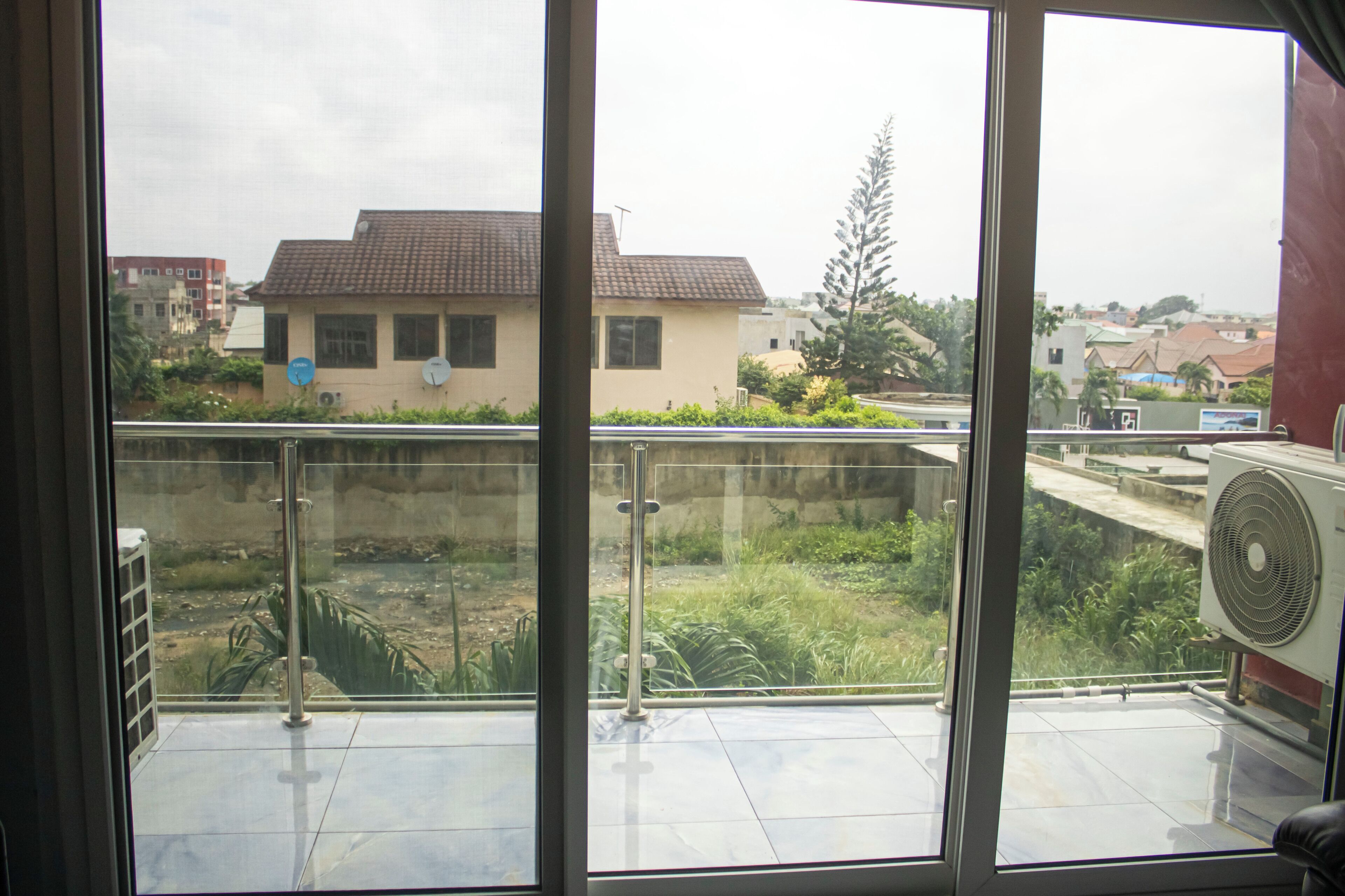 Une vue depuis un balcon doté d’une rambarde en métal, d’un ventilateur et, au fond, d’un bâtiment avec un toit recouvert de tuiles.