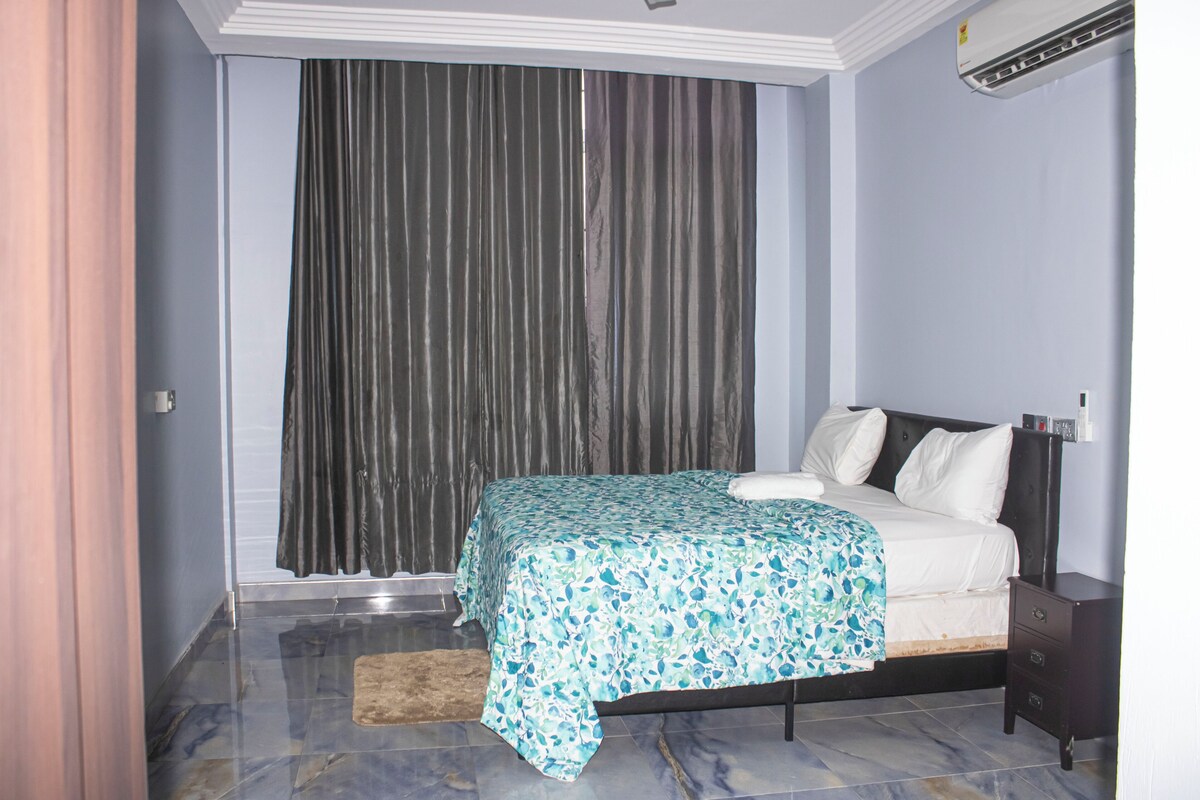 Un dormitorio con cama, mesita de noche, cómoda, ventana con cortinas y equipo de aire acondicionado.