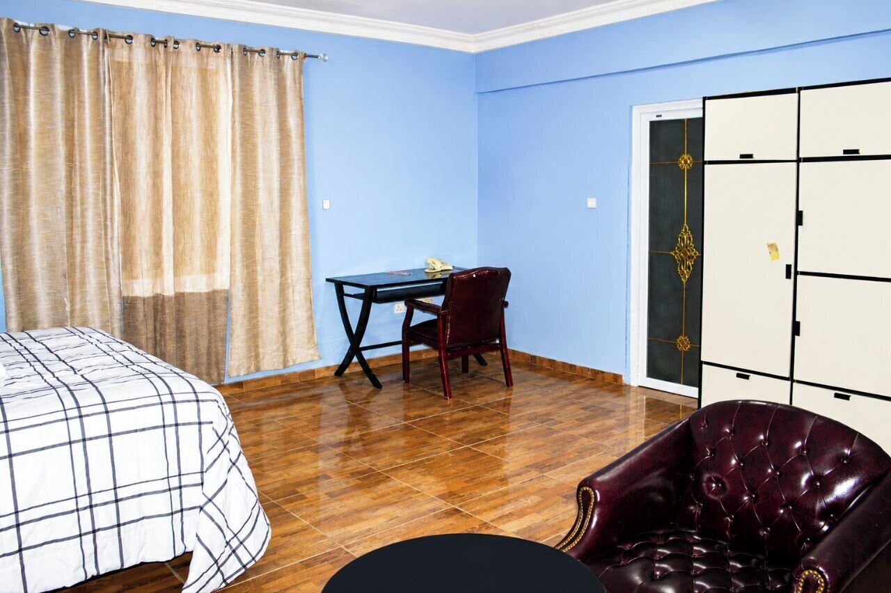 Een kamer met een bed, een bureau met stoel, een kledingkast en een leren fauteuil.