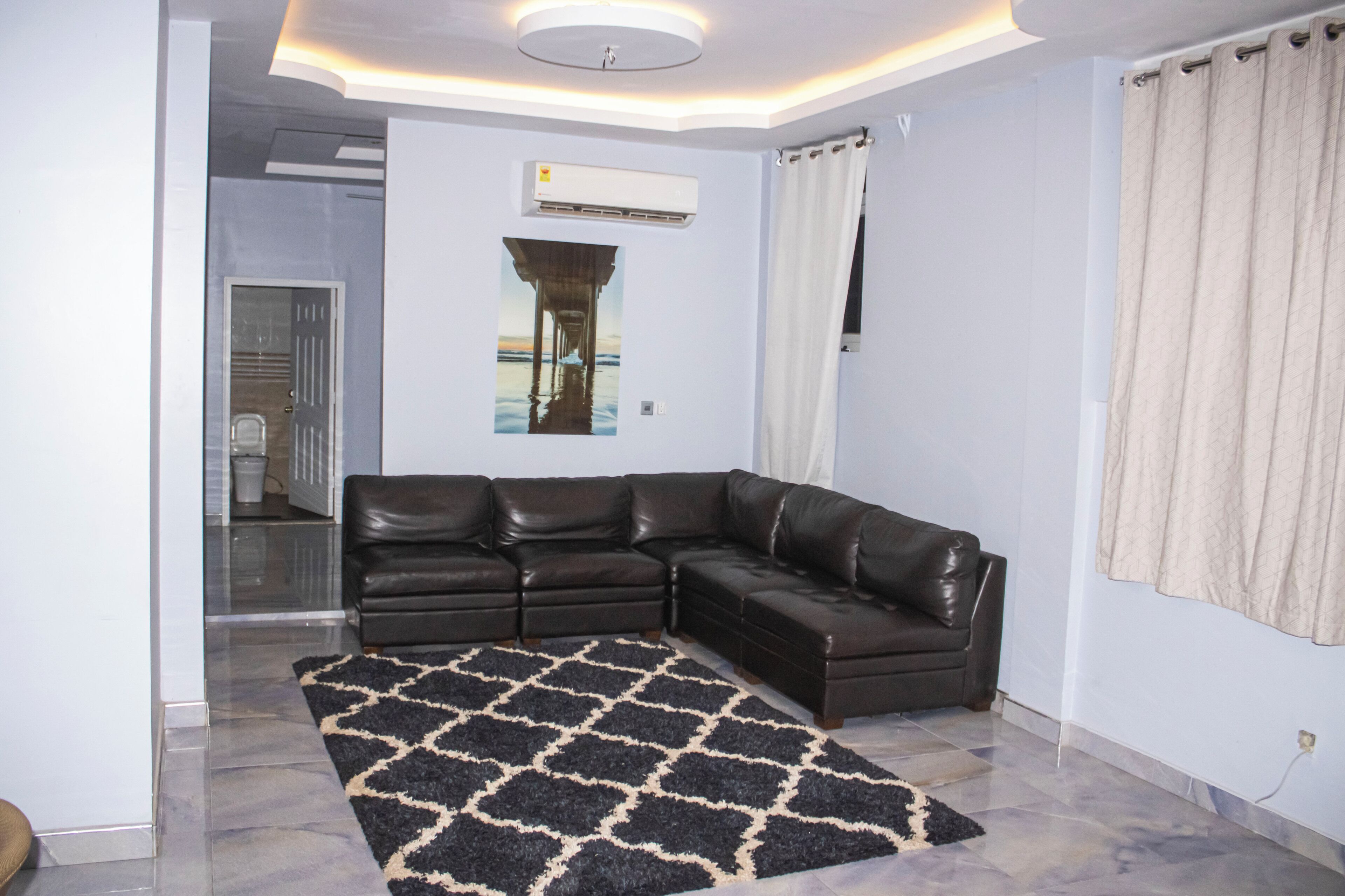 Sala de estar com sofá de couro preto, tapete estampado, luminária no teto e ar-condicionado fixado na parede.