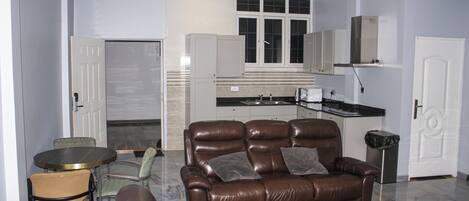 Una sala moderna con un sofá de cuero marrón, una mesa de comedor con sillas, y una cocina con armarios blancos y encimera negra.