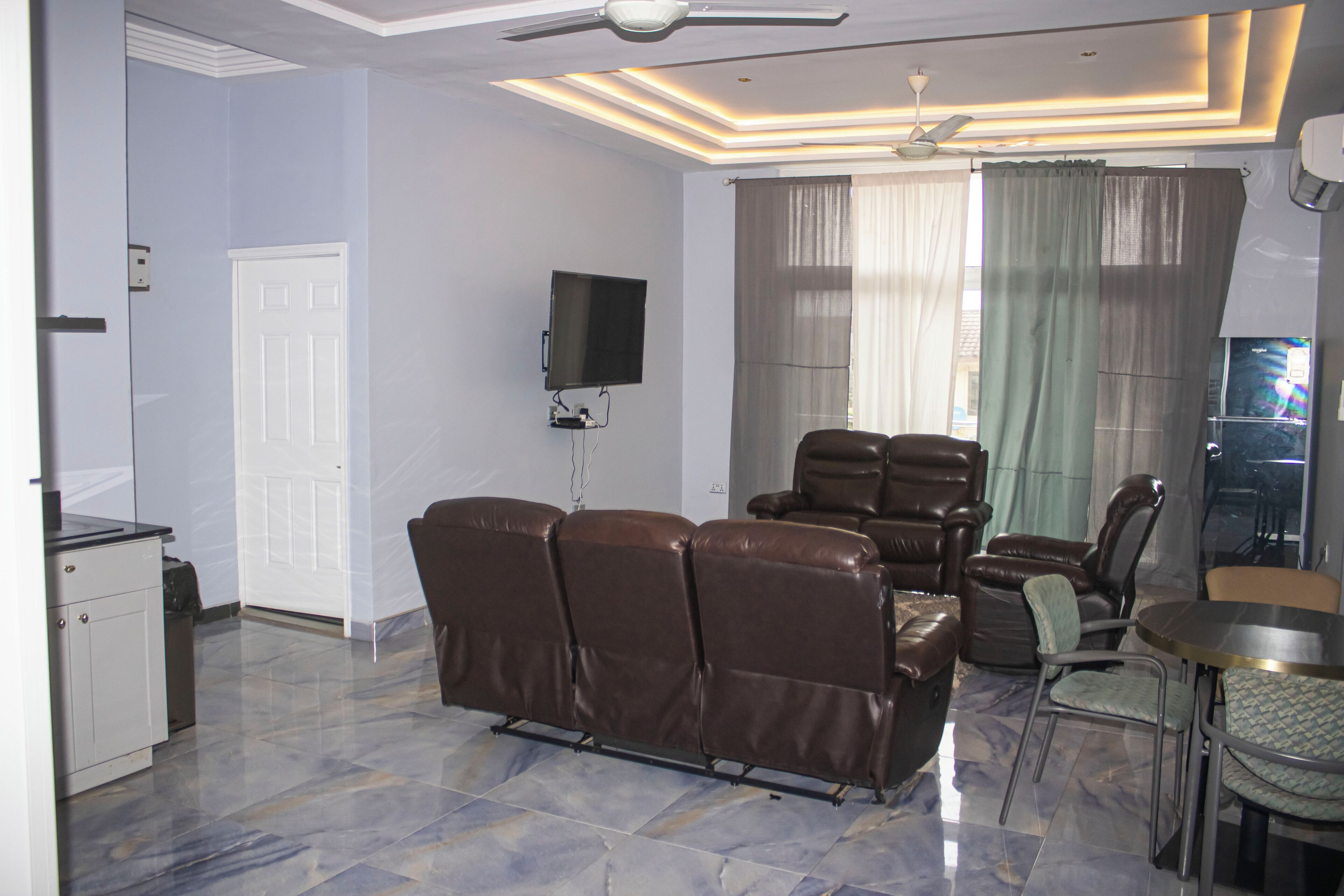 A living room with a reclining sofa, a television mounted on the wall, and a ceiling fan.