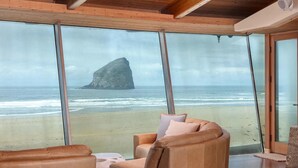 Una stanza con ampie finestre vista spiaggia e mare, con un divano in pelle e un tavolino rotondo.