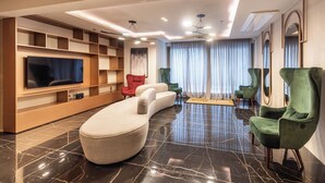 A modern living room with a curved sofa, a flat-screen TV, and a built-in entertainment unit. - StayHome Allianz Park Queen Bed Varanda (São Paulo)