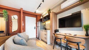 A modern living room with a sofa, a dining area with chairs, a kitchen with a refrigerator, and a TV mounted on the wall. - StayHome Allianz Park Queen Bed Varanda (São Paulo)