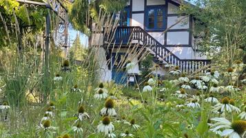 Een traditioneel gebouw met een trap die naar een balkon leidt, omgeven door weelderige begroeiing en witte bloemen.