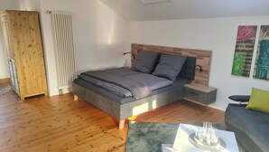 Ein modernes Schlafzimmer mit einem großen Bett, einem Holzkopfende, Nachttischen, einem grauen Sofa und abstrakter Wandkunst.