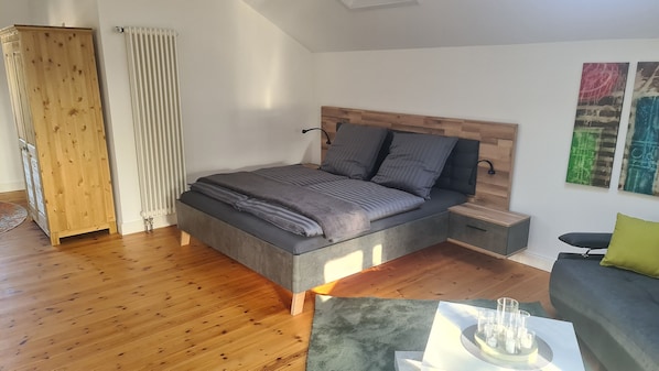 A modern bedroom with a large bed, wooden headboard, bedside tables, a grey sofa, and abstract wall art.