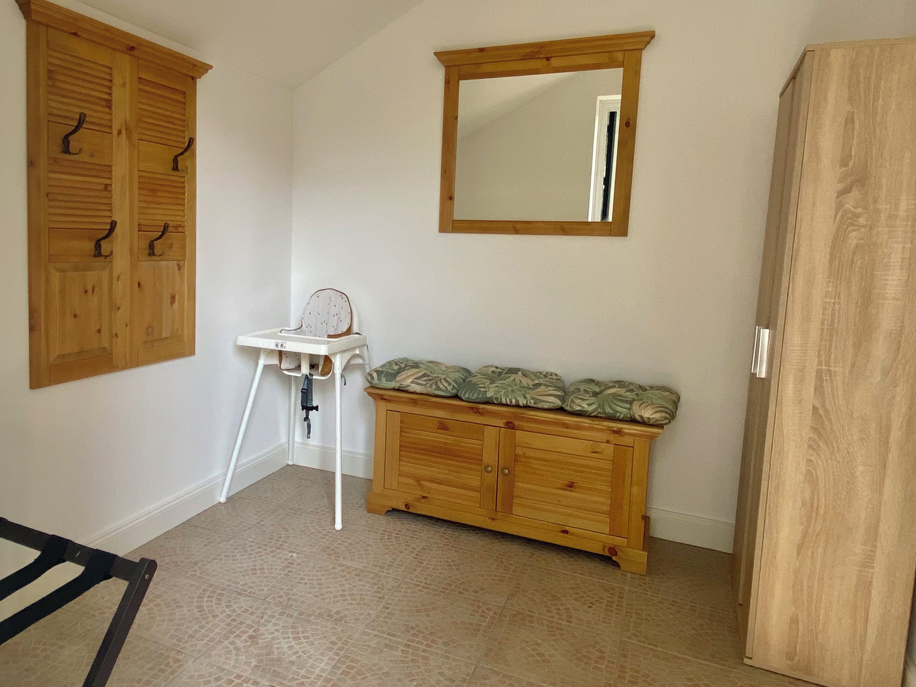 Quarto com um armário de madeira, cadeira alta e espelho na parede.