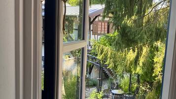 Une fenêtre donnant sur un jardin, avec notamment une terrasse en bois et du mobilier d’extérieur.