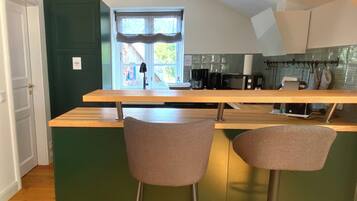 A kitchen with a wooden countertop, two bar stools, a window with curtains, and a green wall.