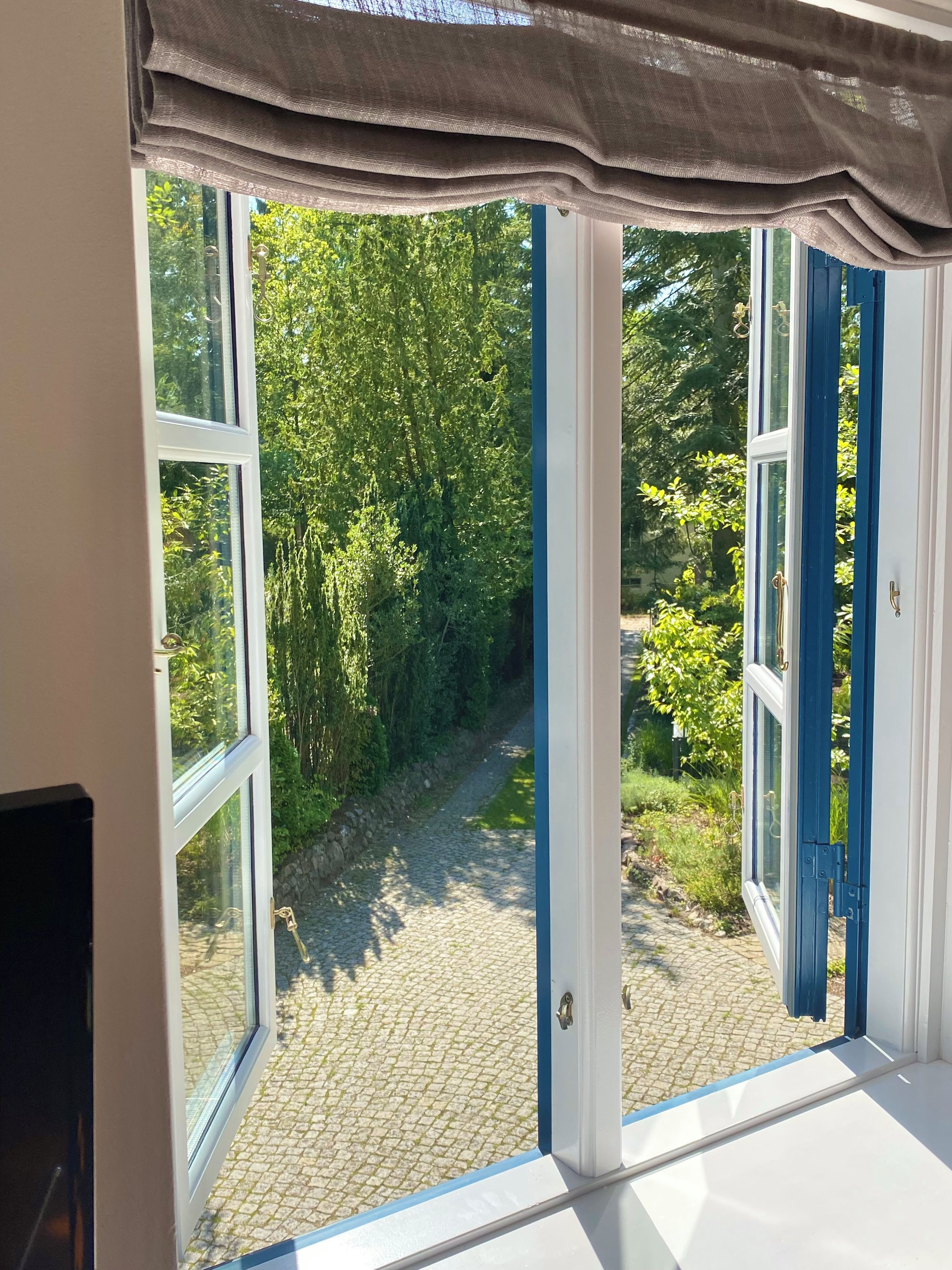 Una habitación con ventanas amplias, vistas a un sendero adoquinado y follaje exterior.