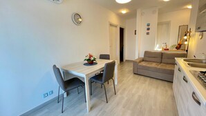 A modern, well-lit living area with a dining table, sofa, and kitchen area. - Bright Apartment With Balcony (Caorle)