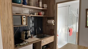 A compact kitchen with wooden cabinetry, a built-in microwave, and a sink. - Lovely studio in mas provençal with private parking (Avignon)