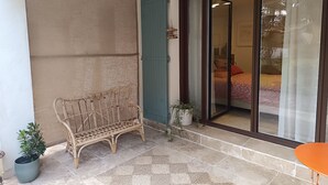 A room with a wicker bench, a small potted plant, a patterned rug, and a sliding glass door leading to another room. - Lovely studio in mas provençal with private parking (Avignon)