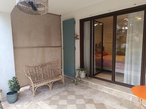 A room with a wicker bench, a small potted plant, a patterned rug, and a sliding glass door leading to another room. - Lovely studio in mas provençal with private parking (Avignon)