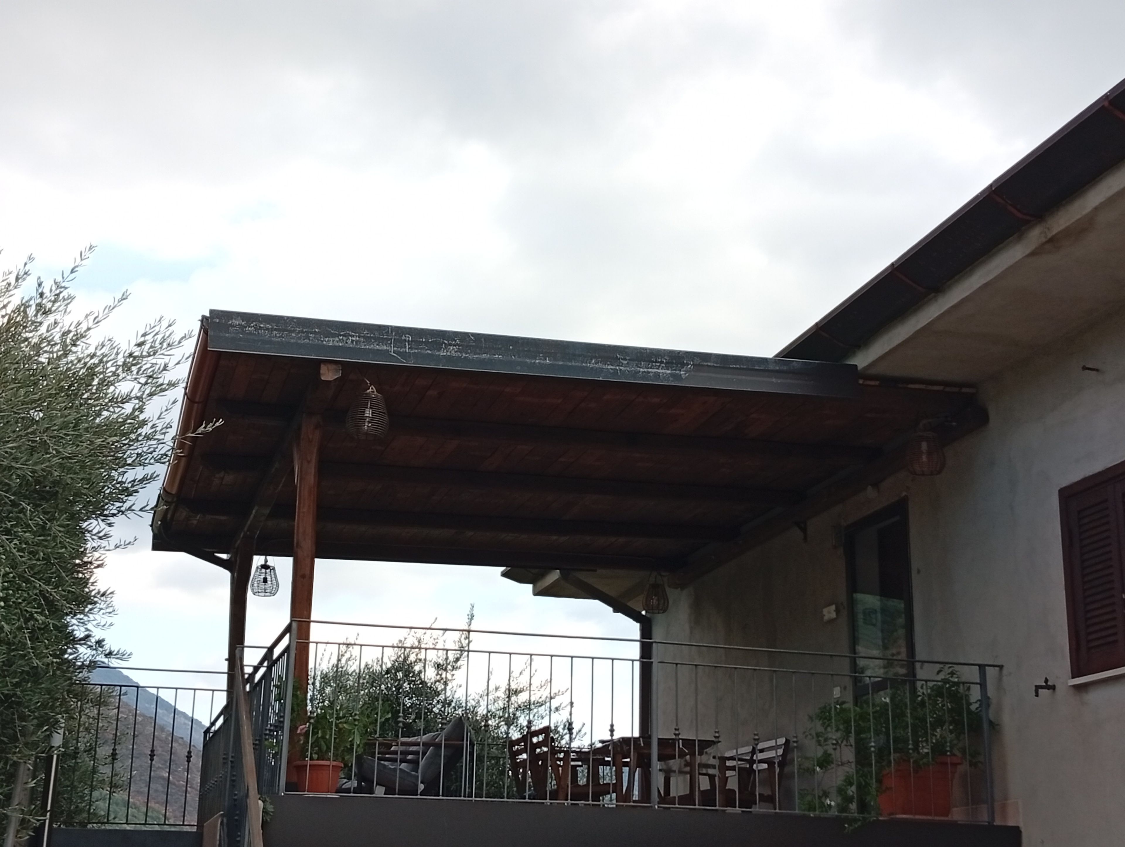 Un'area esterna riparata con tetto in legno, ringhiera in metallo e piante in vaso.