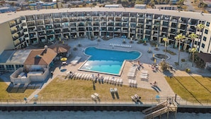 A hotel with a pool surrounded by lounge chairs and umbrellas, a covered seating area, and a view of the surrounding neighborhood. - Hawaiian Inn 502 (Daytona Beach Shores)
