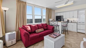 A modern living room with a red sofa, a white wicker coffee table, and a ceiling fan. - Hawaiian Inn 502 (Daytona Beach Shores)
