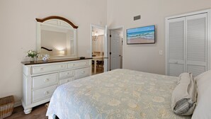 A bedroom with a bed, dresser, mirror, and a painting of a beach scene. - Sea Woods Villa 277 (New Smyrna Beach)
