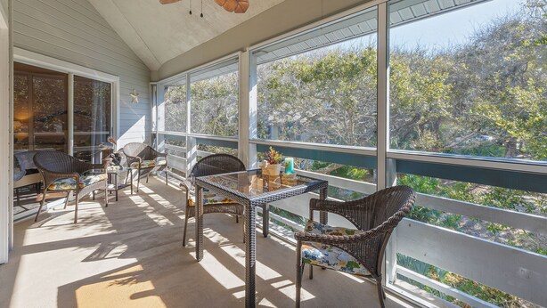 A sunlit balcony with wicker furniture, a ceiling fan, and large windows offering a view of trees. - Sea Woods Villa 277 (New Smyrna Beach)