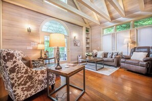 A cozy living room with wooden walls, a large arched window, and a ceiling with exposed beams. - Mountain View Hideaway | Hot Tub + EV Charger (Pigeon Forge)