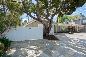 A residential property with a stone driveway, a white fence, and a large tree providing shade.