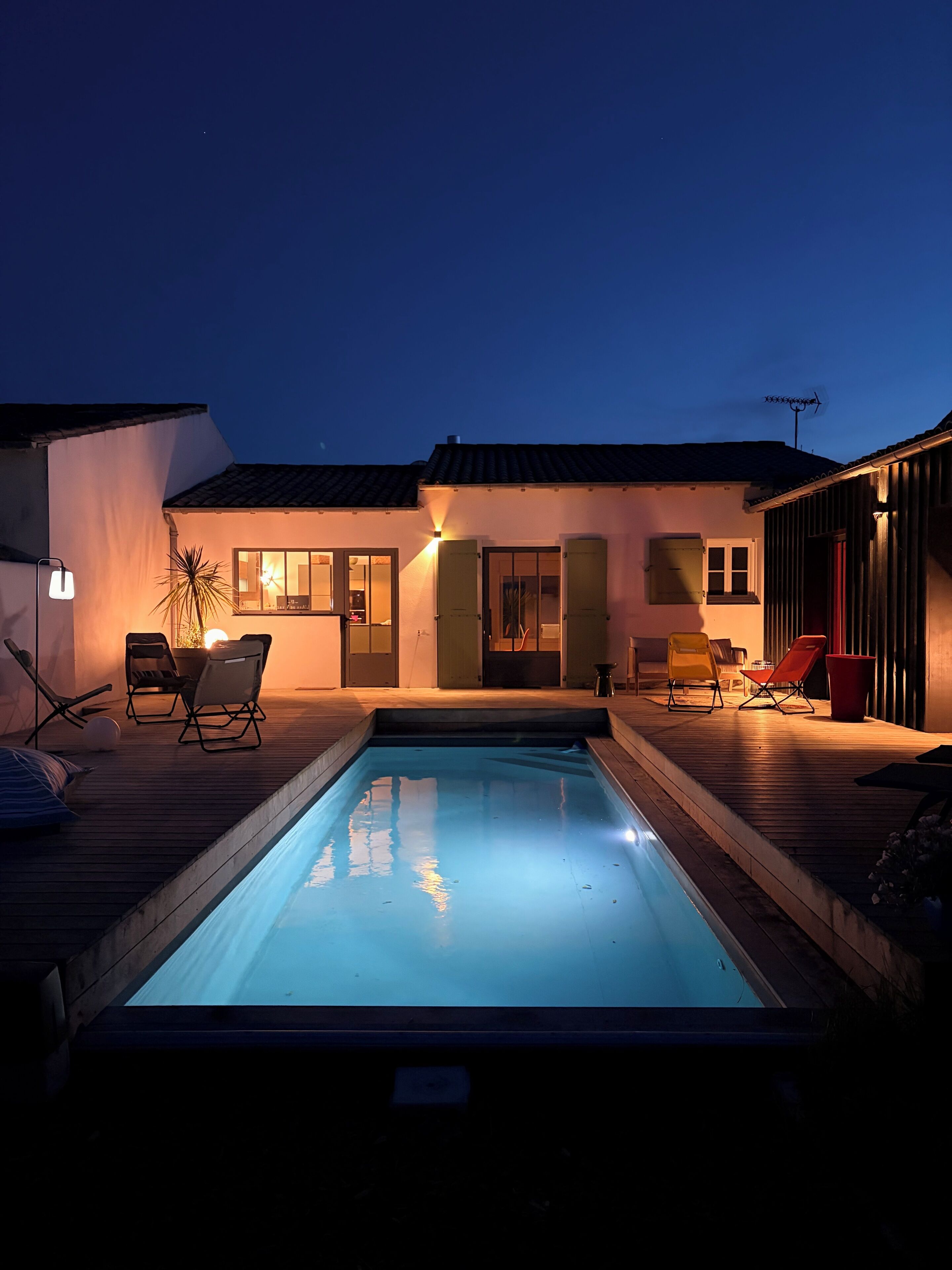 A swimming pool with lounge chairs, a small deck, and a building with a tiled roof.