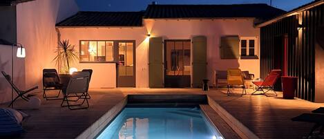 A swimming pool with lounge chairs, a small deck, and a building with a tiled roof.