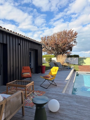 Eine Holzterrasse mit Pool, Liegestühlen und einem kleinen Tisch.