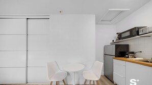 A modern kitchen with white cabinets, a microwave, a coffee maker, and a small dining table with two chairs. - Chic Miami Studio - Gym and Free Parking (North Miami)