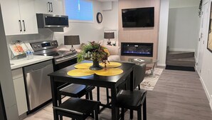Una cocina moderna con electrodomésticos de acero inoxidable, un comedor con una mesa y sillas negras, y un televisor de pantalla plana montado en la pared.