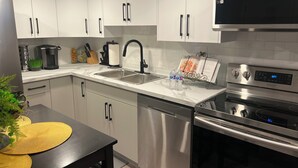 Una cocina moderna con armarios blancos, electrodomésticos de acero inoxidable, un reloj digital y una cafetera.