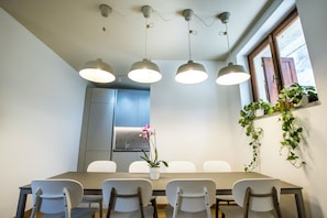 Un salón de conferencias con una larga mesa, sillas blancas, lámparas colgantes, una orquídea en maceta y un ventanal con vistas.