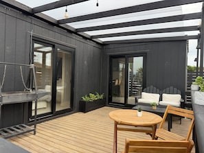 A covered outdoor area with a wooden deck, a table with chairs, and a grill.