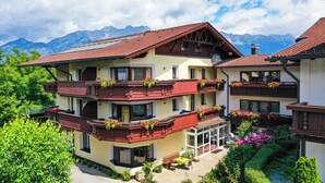 Un immeuble à plusieurs étages doté de balcons, d’un patio aménagé avec des sièges, et ayant une chaîne de montagnes en toile de fond.