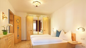 Une chambre à coucher avec un lit en bois, une table de chevet et un miroir. On y trouve une commode avec des tiroirs et une plante en pot.
