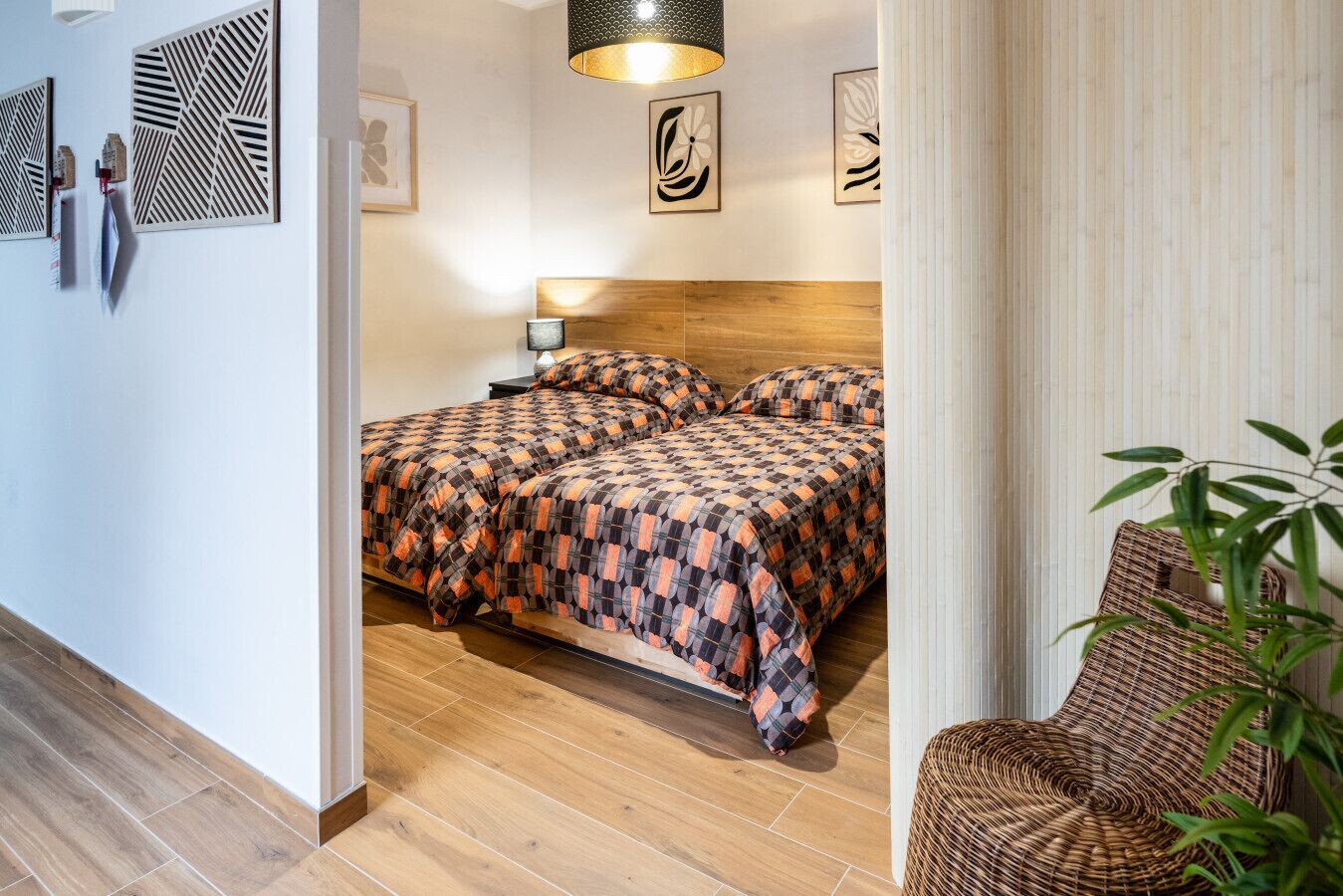 Une chambre d’hôtel avec un plancher en bois, un lit avec une literie à motifs, une table de chevet avec une lampe et des œuvres d’art murales.