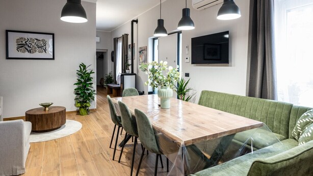 Un'area pranzo moderna con un tavolo in legno, sedie imbottite verdi e lampade a sospensione.