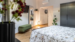 Una camera da letto con un letto, una panca verde, una TV a parete, una sveglia e un armadio.