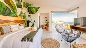A bedroom with a bed, a TV, a balcony with a view, and a large plant. - La Casa Blanca (Puerto Vallarta)