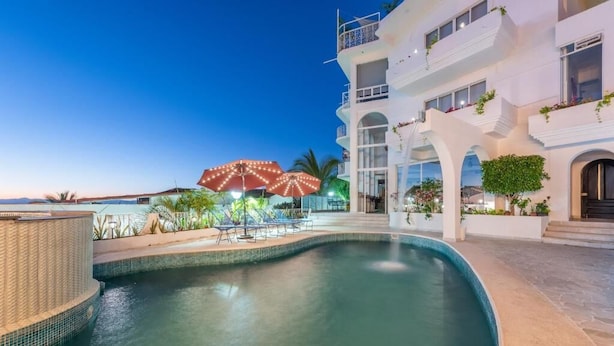 A swimming pool with lounge chairs, umbrellas, and a building with balconies and plants. - La Casa Blanca (Puerto Vallarta)